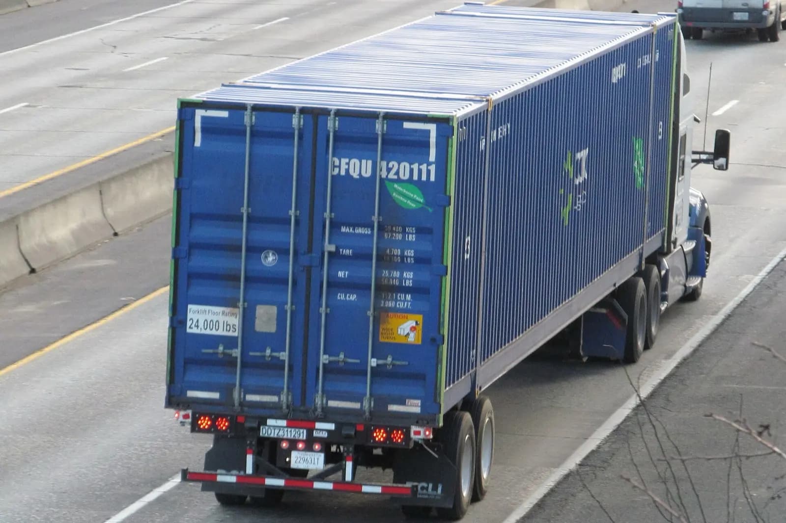 A truck carrying a 40 foot shipping container on a highway